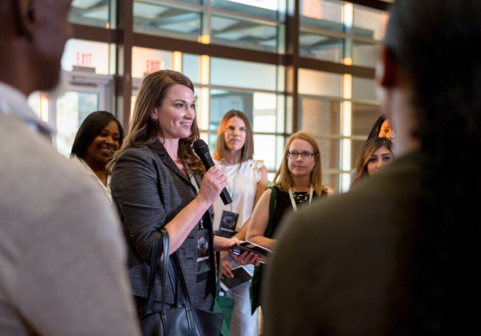 Cheerful mid adult business conference speaker gestures as she answers questions during a Q&amp;A portion of the conference.